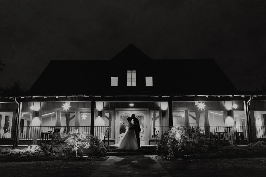 Bride and groom kissing on the steps of a lit barn venue at night